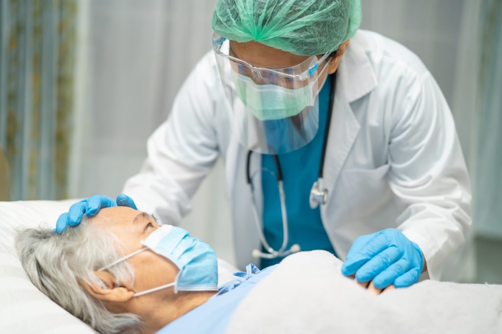 Asian doctor wearing face shield and PPE suit to check elder woman patient protect infection