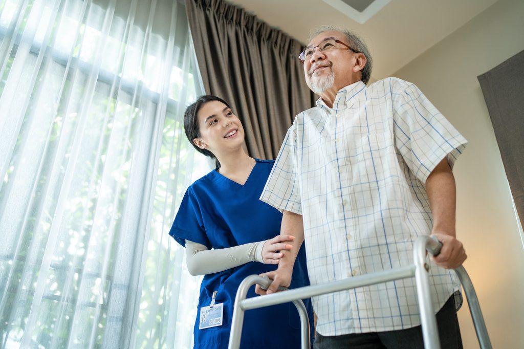 Asian Nurse support elder disable man walk with walker at nursing home.